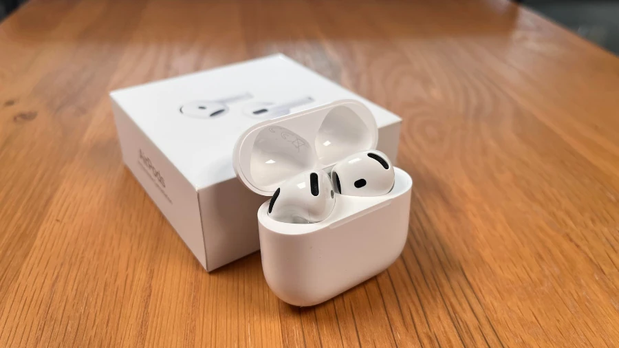 AirPods 4 ANC im geöffneten Ladecase anliegend an der OVP auf einem Holztisch