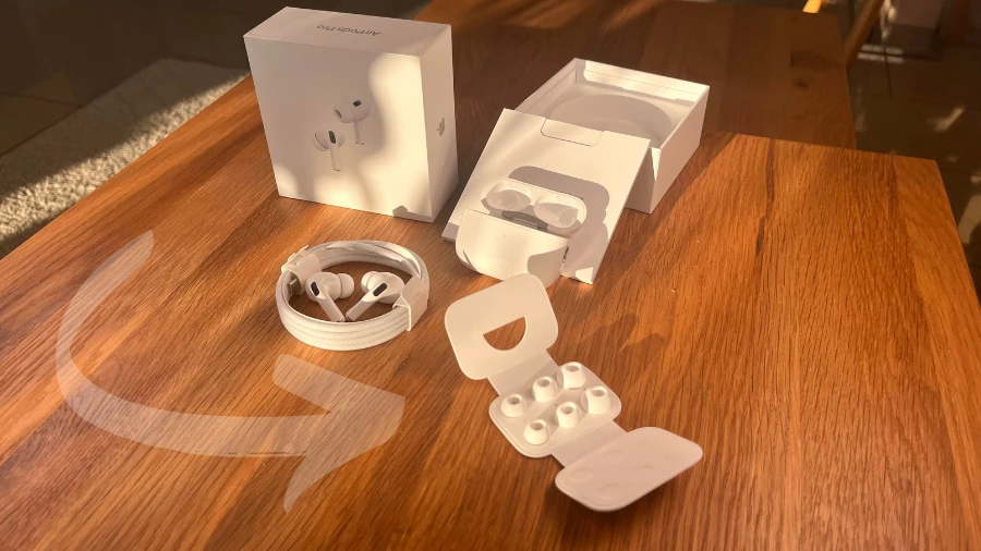 Lieferumfang der AirPods Pro 2 auf einem Holztisch im Wohnzimmer